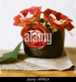 Still life of 3 red roses in vase with linen cloth on wooden table Stock Photo