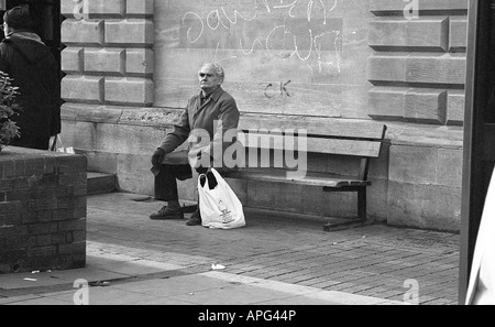 old man sitting on seat outside with shopping bag. Stock Photo