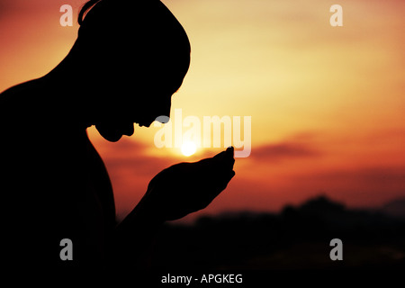 Silhouette of a man with cupped hands below a setting sun Stock Photo