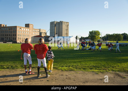 WISCONSIN Racine Two boys in football uniforms watching game in field junior high students playing Stock Photo