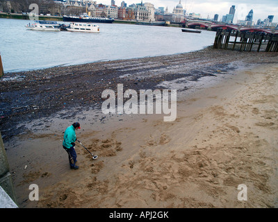 A Man using a metal detector on the south bank of the Thames River. London England UK Stock Photo