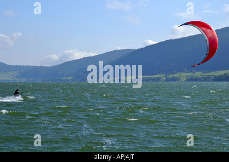 A kite surfer speeds across a mountain lake in Switzerland. Space for text on the sky top left. Stock Photo