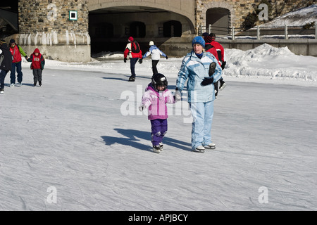 Small boy learning to ice skate He s wearing a helmet with a protective face mask Stock Photo