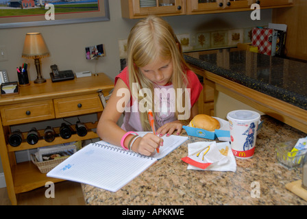 8 year old girl writes in her journal while eating lunch from a fast food restaurant Stock Photo