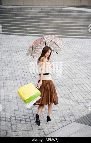 Woman with umbrella and shopping bags walking across public square (rear view, high angle view) Stock Photo