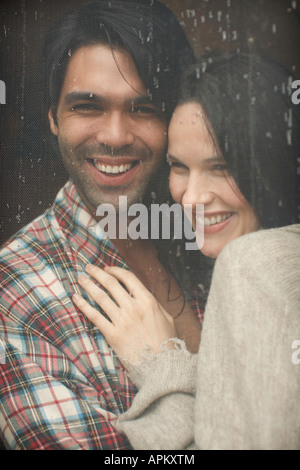 Young couple hugging by window with rain running down Stock Photo