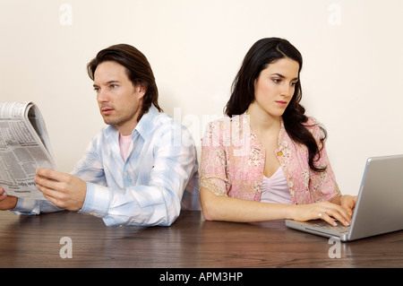 Man reading newspaper and woman using laptop computer Stock Photo