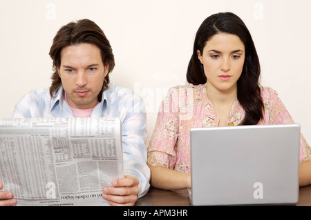 Man reading newspaper and woman using laptop computer Stock Photo