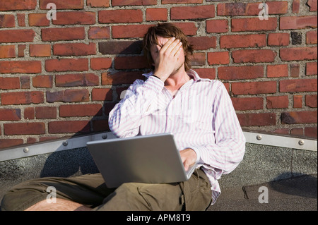 Man using laptop, leaning by wall Stock Photo