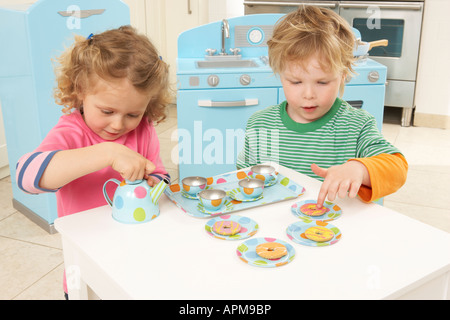 a boy and a girl play in a kitchen with a toy spotty tea set Stock Photo