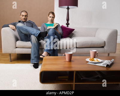 Young woman reading book and young man listening to MP3 player on sofa Stock Photo