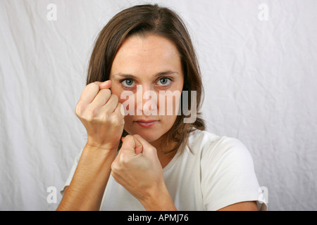 Attractive young woman holds clenched fists up to her face protective violent boxing stance with determined facial expression Stock Photo