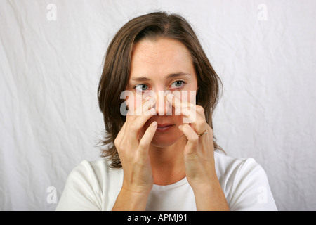 Young brunette woman suffering from head cold and sinus pain rubs sinus area above her nose to gain relief from the pressure Stock Photo