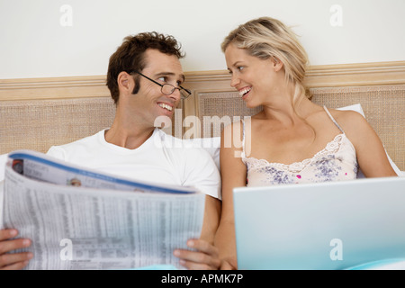 Mid adult couple using laptop and reading newspaper in bed Stock Photo