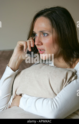 Pretty young 20s 30s woman female looks anxious concerned during a cordless telephone conversation while relaxing at home Stock Photo