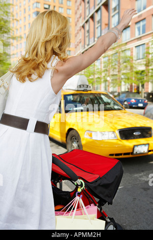 Mid adult woman with shopping bags hailing taxi (rear view), New York City, New York, USA Stock Photo