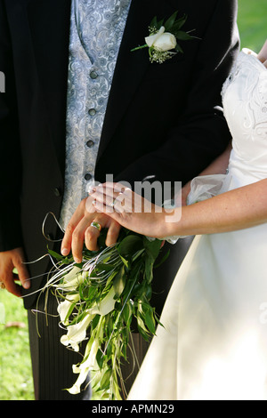 Abstract Bride and Groom closeup showing golden wedding rings bands button hole and brides flowers and white dress England UK Stock Photo