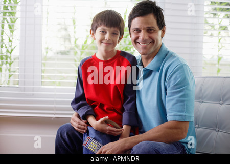 Father and son sitting on armchair, father holding remote control Stock Photo