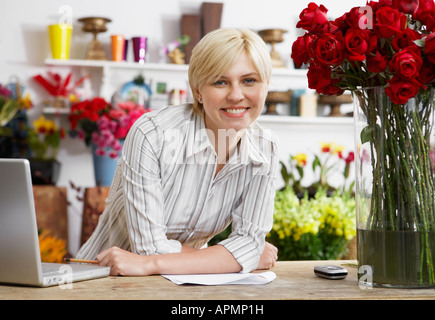 Female florist with laptop leaning on table (portrait) Stock Photo