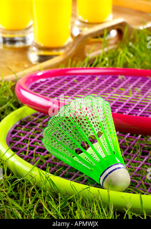 Children's colourful Badminton Racquets and shuttlecock lying on grass with a tray of glasses of Orange Juice in the Background. Stock Photo