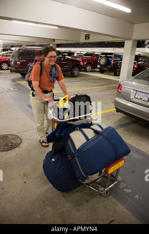Female tourist pushing airport trolly laden with bags through car hire parking area Vancouver Canada Stock Photo