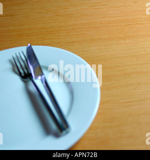 Empty clean dinner plate with knife and fork on tabletop Stock Photo