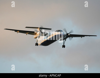 Short haul air travel. Bombardier Dash 8-Q300 twin engine propeller powered passenger plane flying on approach at sunset. No airline titles visible. Stock Photo