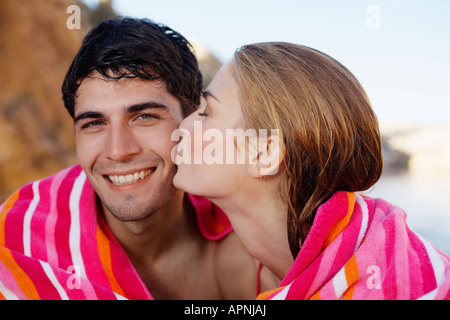 Young couple wrapped in a towel, woman kissing man on cheek Stock Photo