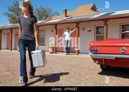 Girlfriend leaving motel, boyfriend looking  in background Stock Photo