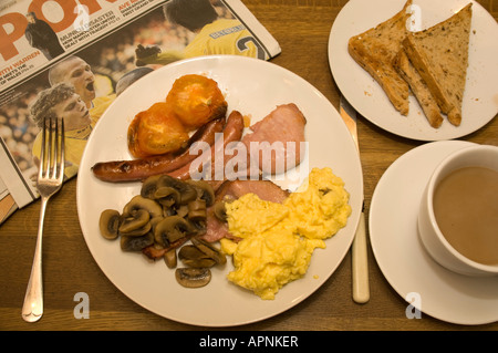 full english cooked breakfast bacon egg and sausage toast coffee tomato newspaper on wooden dining room table Stock Photo