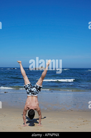 Young Man Standing on Hands on Sandy Beach Stock Photo