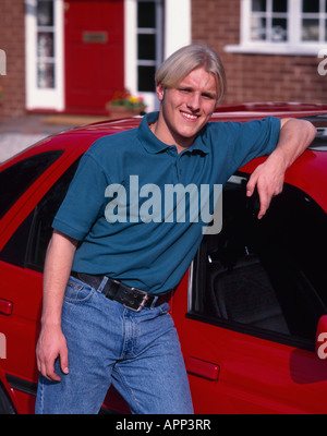 Young man smiling leaning on a [red car] England Stock Photo