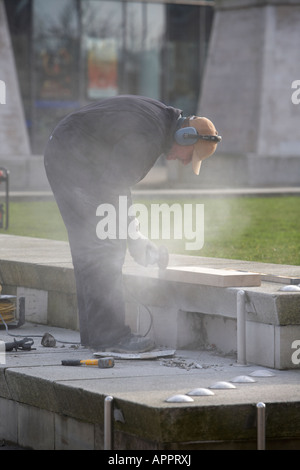 man cutting stone with an angle grinder repairing pedestrian area of Belfast Northern Ireland UK Stock Photo