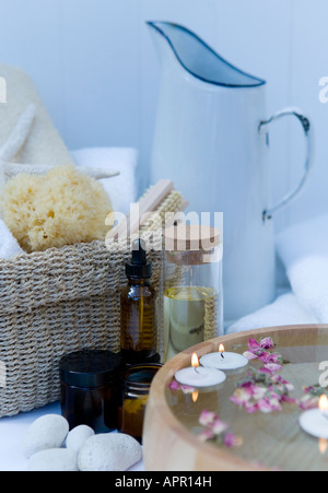 Spa bathroom setting: aromatherapy oils, vintage enamel jug, natural sponge, wooden bowl filled with water and floating petals Stock Photo