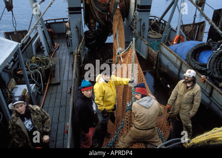 commercial fisherman fix a net on a small factory trawler as they hide from a storm in Kodiak Alaska Stock Photo