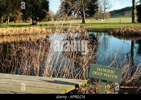 Pond in late winter with 'Danger Deep Water' warning sign at the edge. West Dean Gardens,Sussex, England, UK Stock Photo