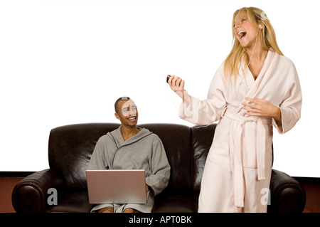 couple sitting on the sofa using a laptop and listening to an ipod and playing air guitar Stock Photo
