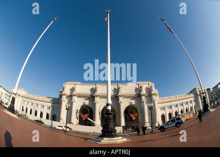 Union Station Exterior Washington DC | WASHINGTON D.C., United States — A fisheye view of Union Station's curved Beaux-Arts facade stretches beneath tall flagpoles topped with gilded eagles. Completed in 1908 to designs by architect Daniel Burnham, the station remains Washington's principal railway gateway, with holiday wreaths hung across its central arches. Stock Photo