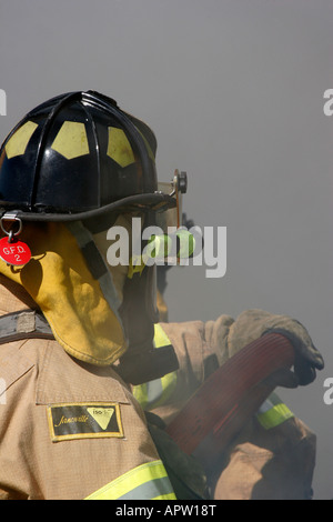 Two firefighters using a hoseline to extinguish a car fire while being surrounded by smoke and spray Stock Photo