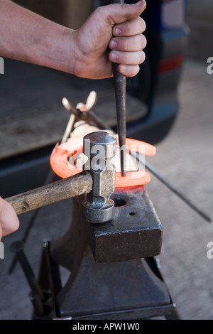 Farrier shaping molten horse shoe on anvil Stock Photo