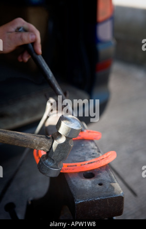 Farrier shaping molten horse shoe on anvil Stock Photo