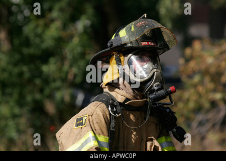 An American firefighter investigating a structure fire while holding onto a hoseline pumping and spraying water Stock Photo