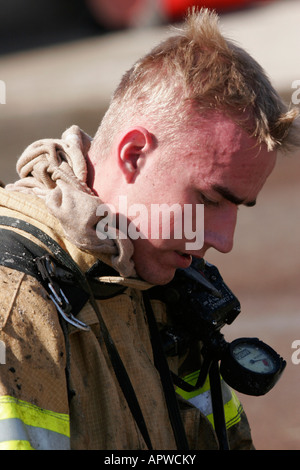 A young male firefighter full of debris is taking off his protective gear after putting out a structure fire Stock Photo