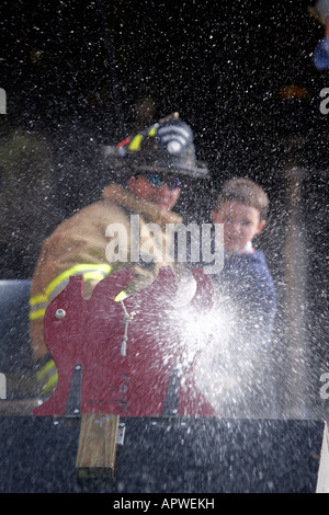 A Mequon Fire Department Firefighter and a young boy using a hoseline to spray water on a house fire Stock Photo