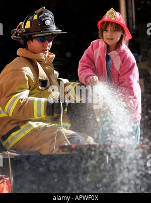 A Mequon Fire Department Firefighter and a young girl using a hoseline to spray water on a house fire demonstration Stock Photo