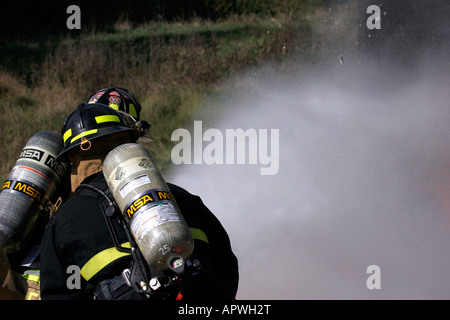 Two American firefighters with a hoseline spraying water towards a fire Stock Photo