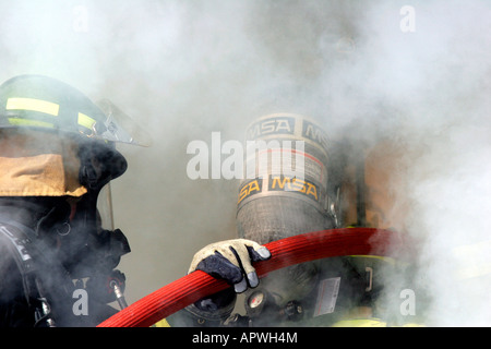 Two firefighters with a hoseline entering smoke billowing from a structure fire Stock Photo