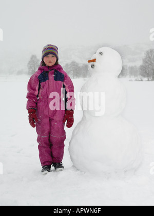 Girl standing next to snowman Stock Photo