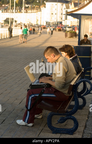 Two polish young people using laptops to access wireless network Aberystwyth promenade Wales UK Stock Photo