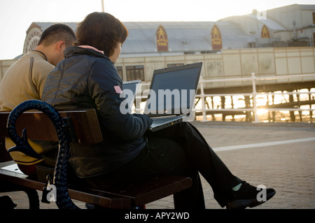 two polish young people using laptops to access wireless network Aberystwyth promenade to call home on Skype and send e-mail Stock Photo